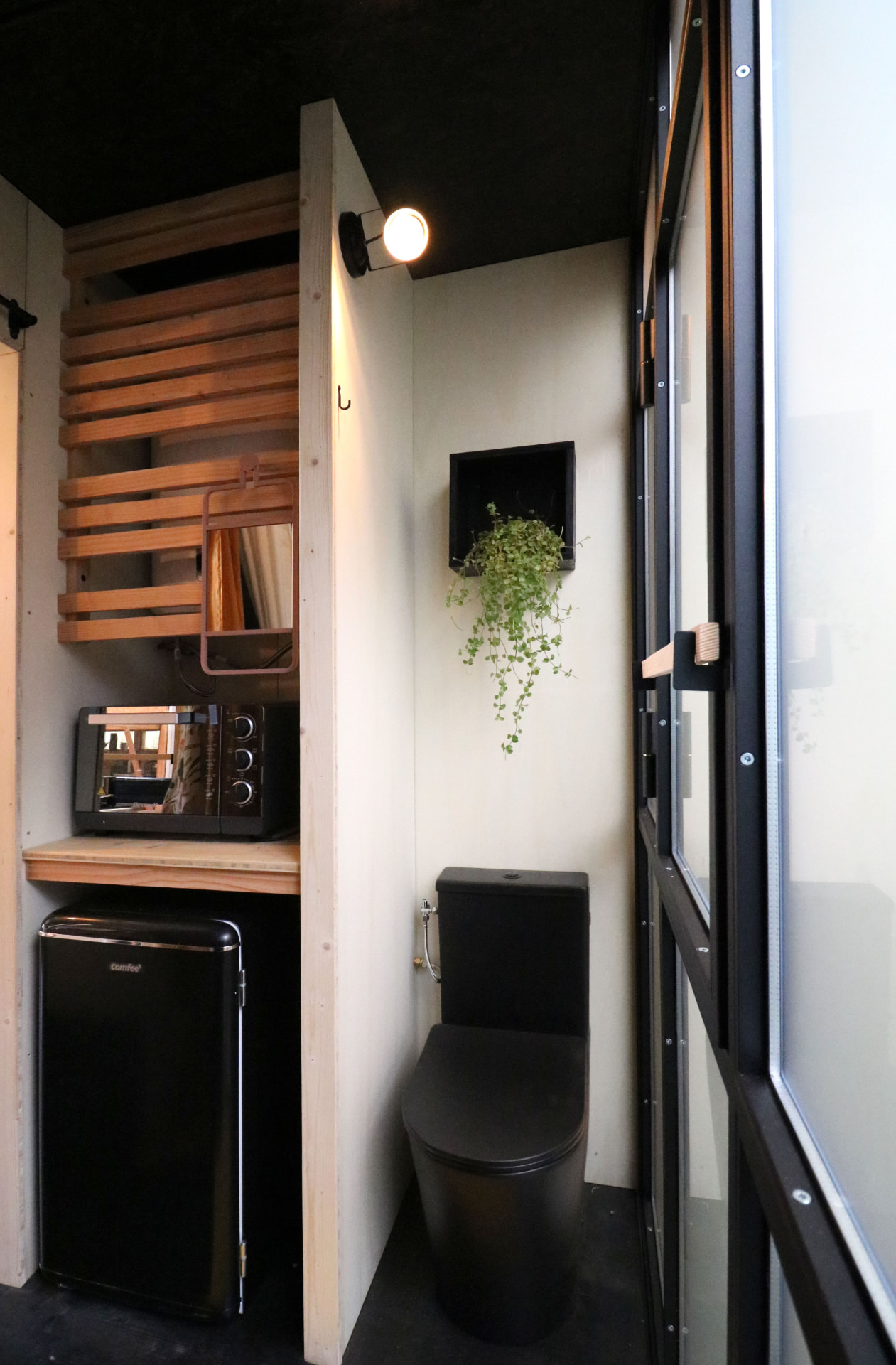 Coin salle d'eau de la PATiny : WC noir, frigo et micro-onde intégrés en bois clair