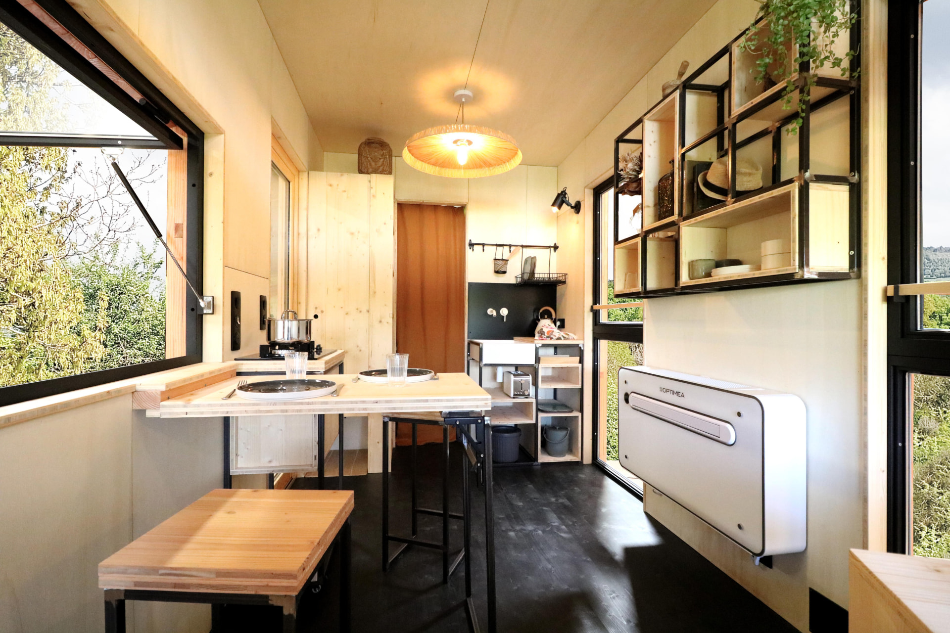 Kitchenette de la PATiny avec table repliable, baies vitrées ouvertes sur la nature